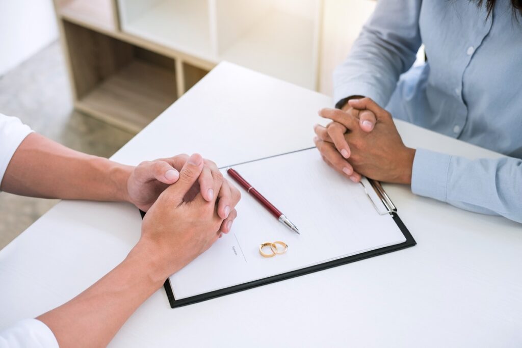 Two people signing divorce documents with wedding rings and legal papers wondering How Long does a divorce take