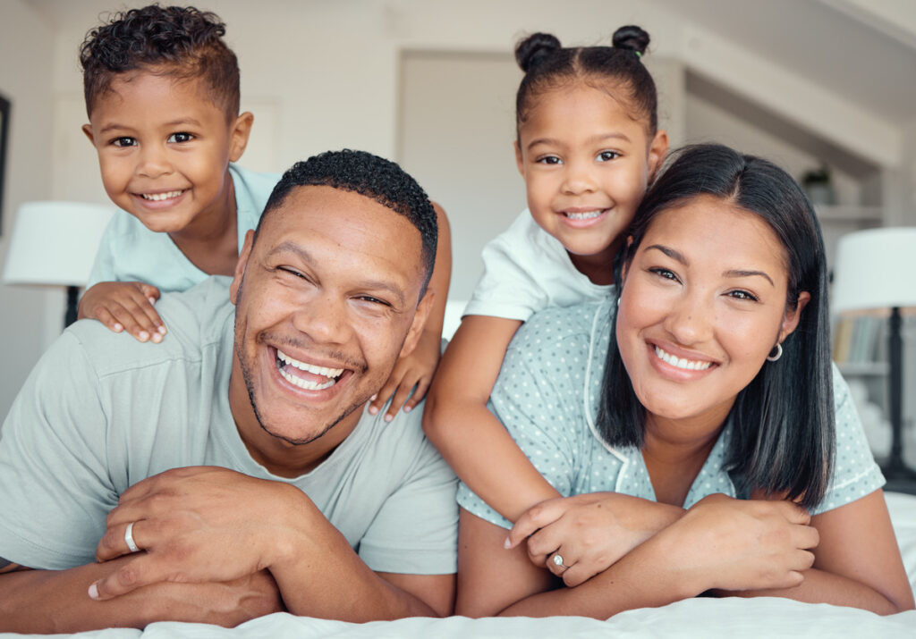 Family of four lying on a bed in a casual setting, illustrating what is the difference between legal separation and divorce. This image captures a moment of togetherness, emphasizing the importance of understanding marital legal options