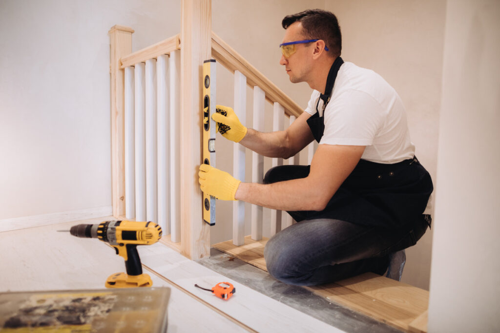 A man in a white shirt and yellow gloves repairs a stair rail, highlighting premises liability in maintenance safety