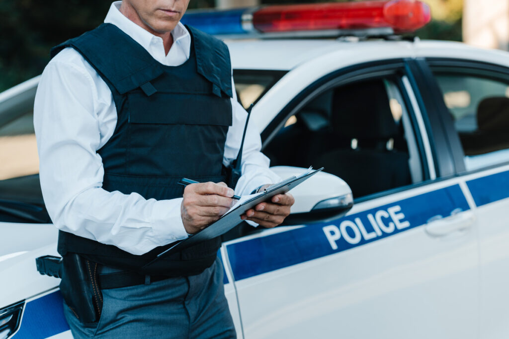 A police officer is seen writing on a clipboard, capturing essential information regarding a car accident report