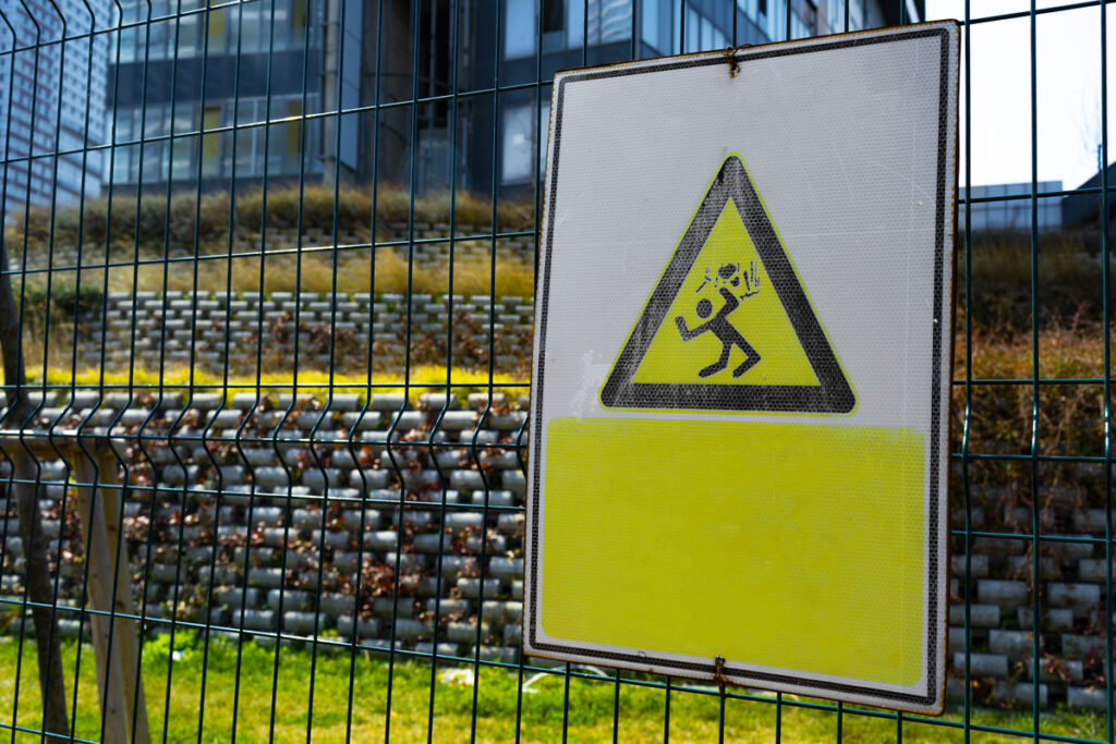 A yellow and black warning sign affixed to a fence, indicating potential hazards on the premises preventing premises liability