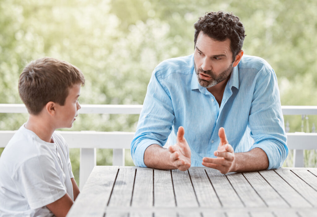 A man and a boy engaged in conversation at a table, fostering a positive and supportive relationship