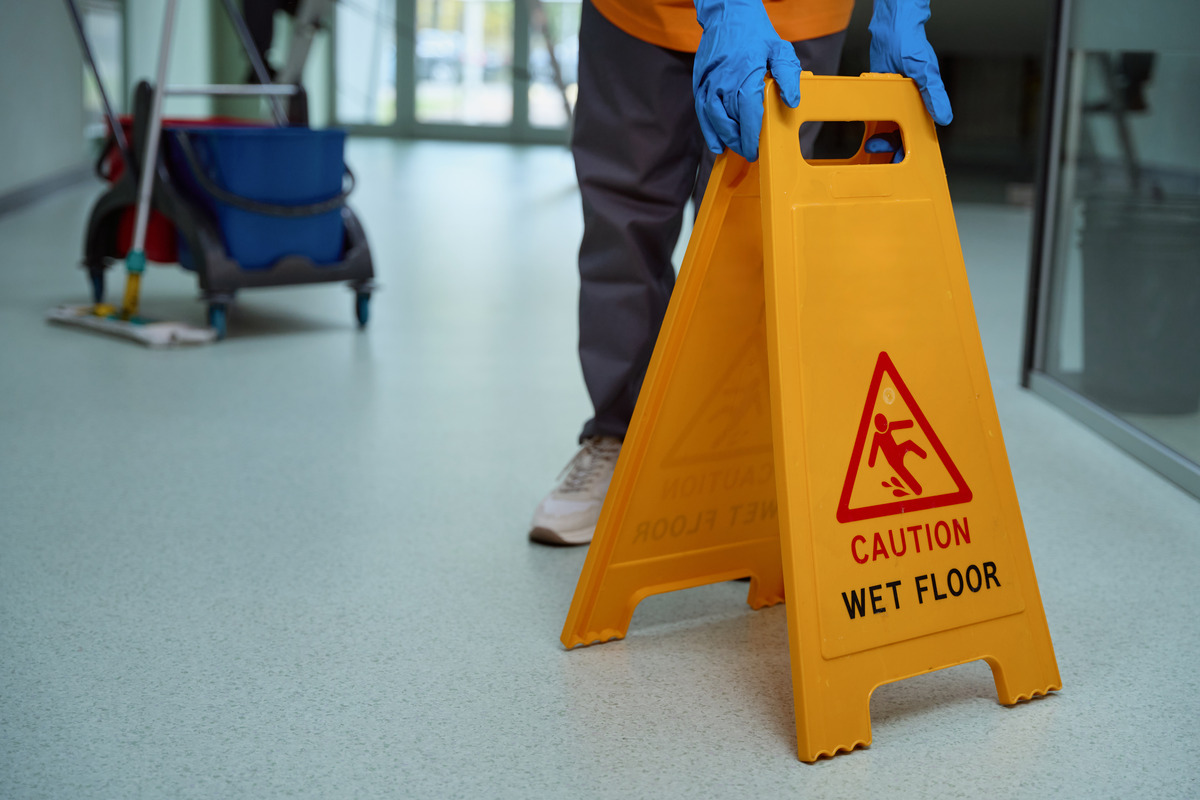 A person in blue gloves holds a wet sign, emphasizing safety after a slip and fall accident