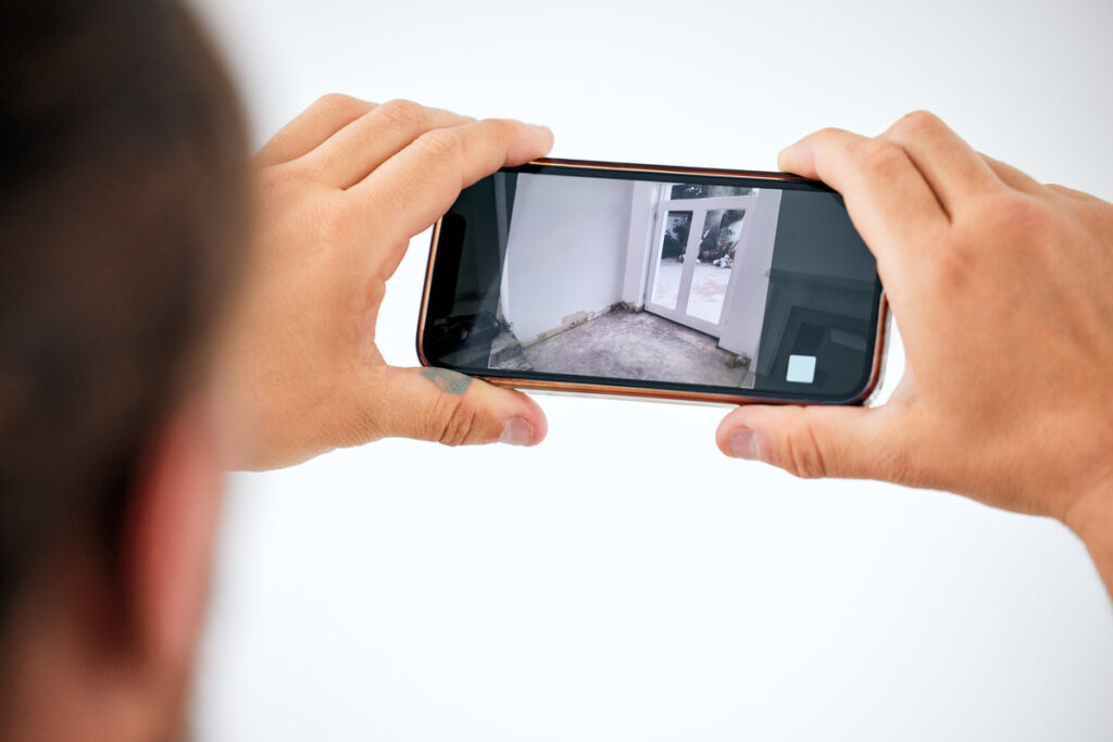 A man photographing a room with his phone, illustrating steps to take after a slip and fall accident