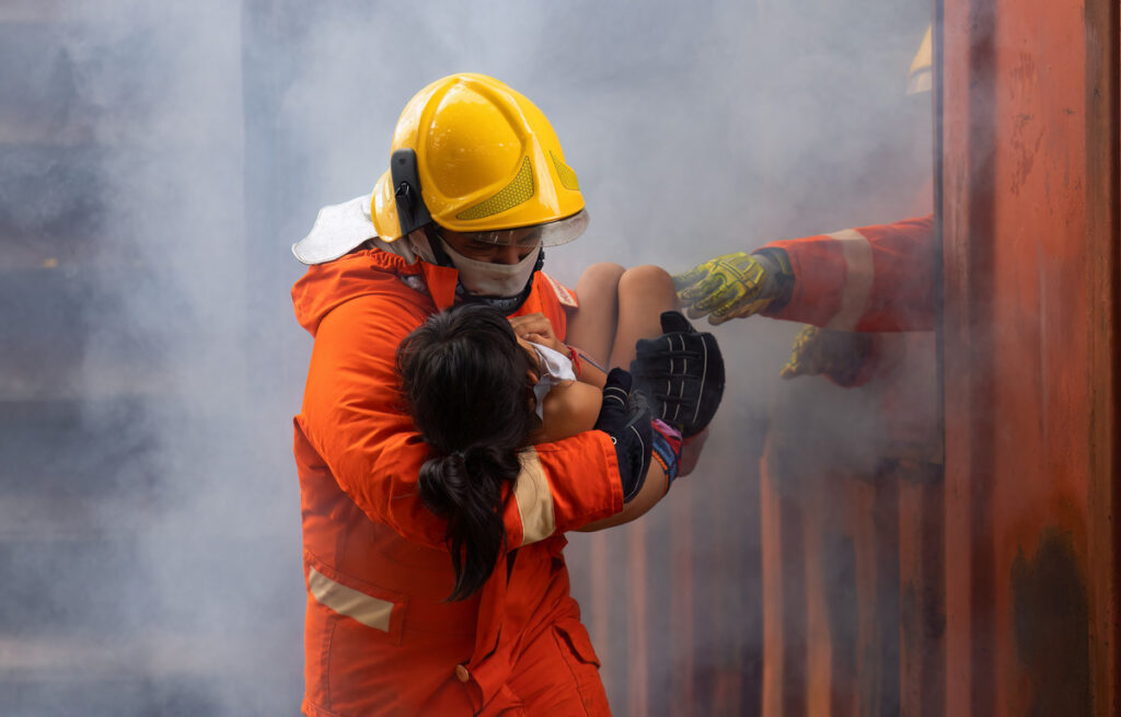 A firefighter assists a child in escaping a smoke-filled room, showcasing bravery and rescue in a dangerous situation
