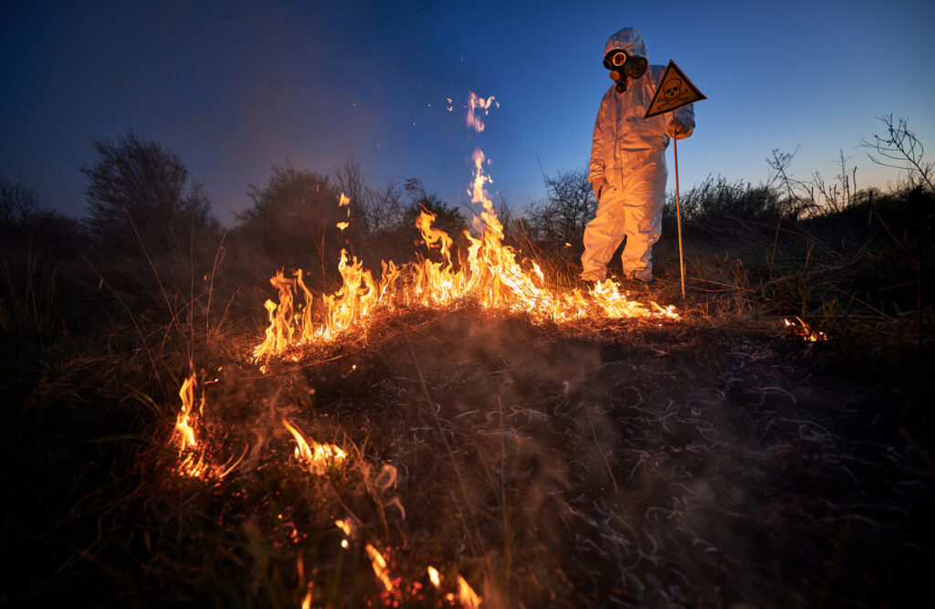 A man in a white suit stands beside a large pile of fire, symbolizing the serious implications of arson