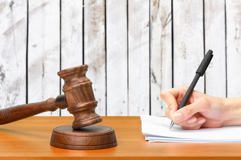 A lawyer's hand writing on paper with a pen, accompanied by a gavel, symbolizing property division legal work