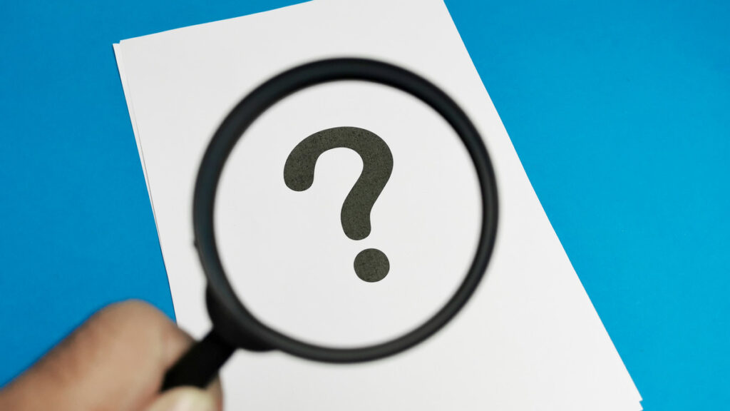 A hand holding a magnifying glass over a paper with a question mark, symbolizing legal inquiries in property division