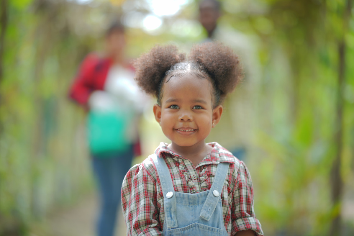 A young girl with afro hair stands joyfully in a vibrant green field, embodying innocence and happiness