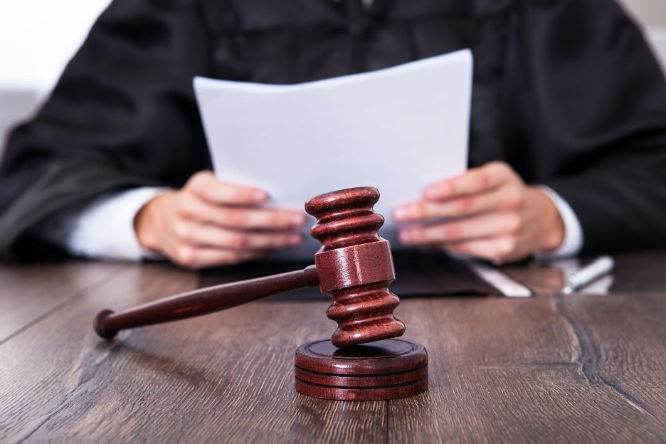 A gavel with the judge reading a case in the background