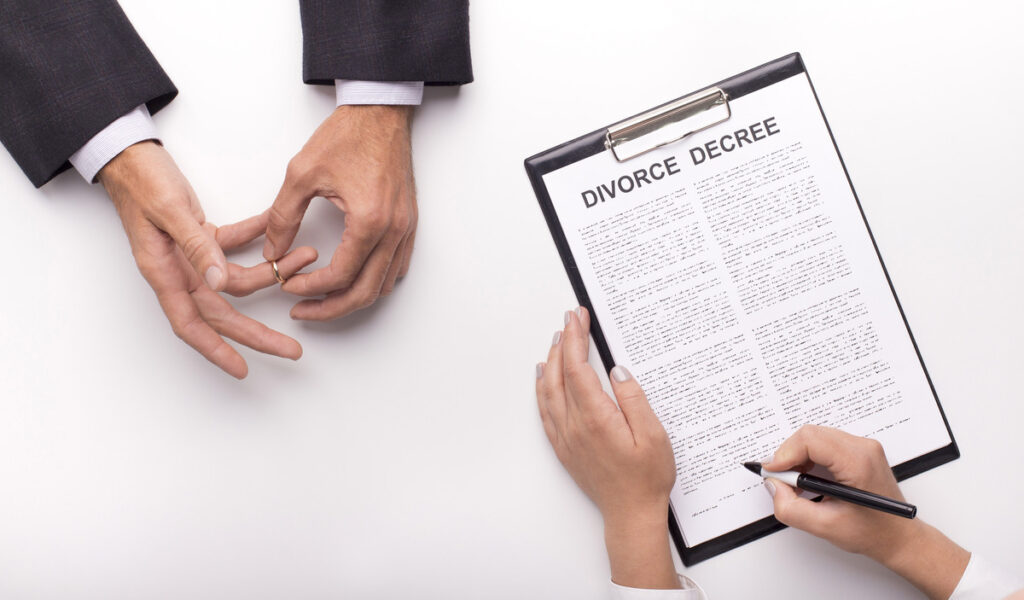 a divorce decree document being signed while a person taking off the wedding ring